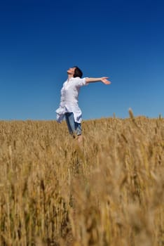 Young woman standing jumping and running  on a wheat field with blue sky in  background at summer day representing healthy life and agriculture concept