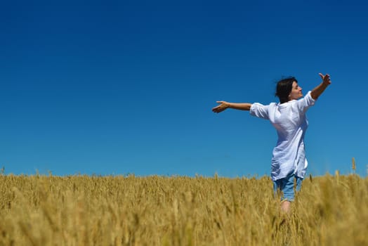 Young woman standing jumping and running  on a wheat field with blue sky in  background at summer day representing healthy life and agriculture concept