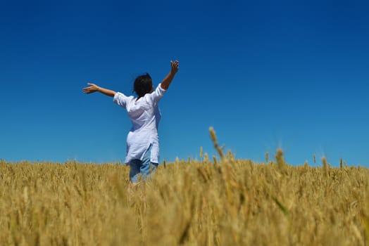 Young woman standing jumping and running  on a wheat field with blue sky in  background at summer day representing healthy life and agriculture concept