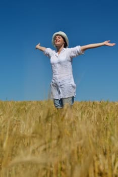 Young woman standing jumping and running  on a wheat field with blue sky the background at summer day representing healthy life and agriculture concept