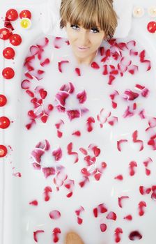 woman beauty spa and wellness treathment with red flower petals in bath with milk 