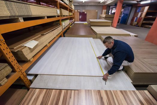 young man carpenter measuring wooden board for cutting while working in big modern carpentry High quality wood concept