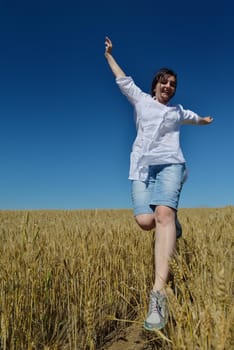 Young woman standing jumping and running  on a wheat field with blue sky the background at summer day representing healthy life and agriculture concept