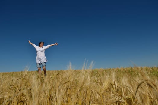 Young woman standing jumping and running  on a wheat field with blue sky the background at summer day representing healthy life and agriculture concept