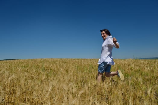 Young woman standing jumping and running  on a wheat field with blue sky the background at summer day representing healthy life and agriculture concept