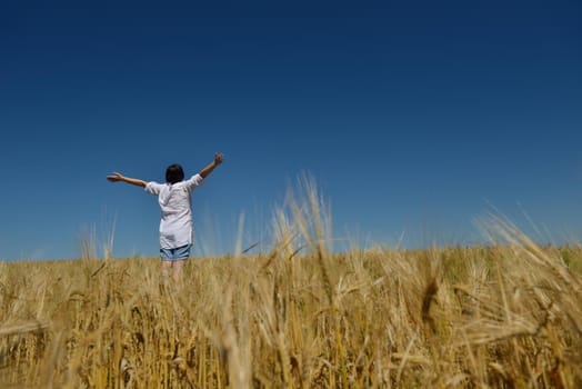 Young woman standing jumping and running  on a wheat field with blue sky the background at summer day representing healthy life and agriculture concept