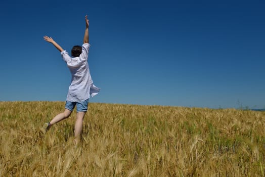 Young woman standing jumping and running  on a wheat field with blue sky the background at summer day representing healthy life and agriculture concept