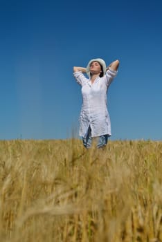 Young woman standing jumping and running  on a wheat field with blue sky the background at summer day representing healthy life and agriculture concept