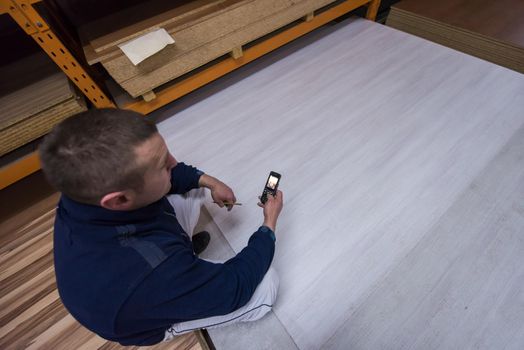 young man carpenter using a mobile phone to calculate measures for wooden board while working in big modern carpentry High quality wood concept