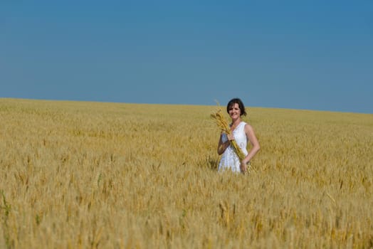 Young woman standing jumping and running  on a wheat field with blue sky the background at summer day representing healthy life and agriculture concept