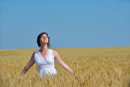 Young woman standing jumping and running  on a wheat field with blue sky the background at summer day representing healthy life and agriculture concept