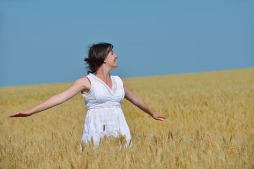 Young woman standing jumping and running  on a wheat field with blue sky the background at summer day representing healthy life and agriculture concept