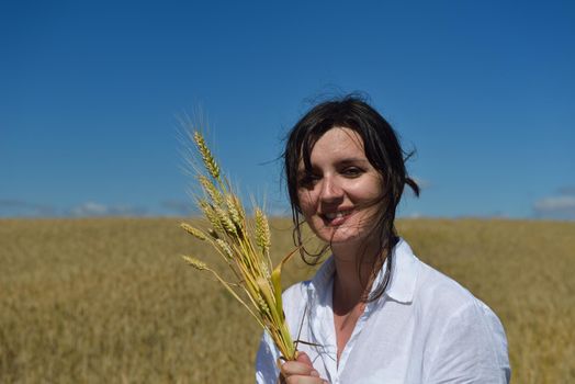 Young woman standing jumping and running  on a wheat field with blue sky the background at summer day representing healthy life and agriculture concept