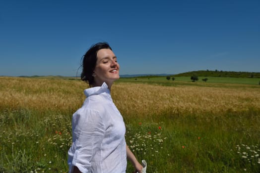 Young woman standing jumping and running  on a wheat field with blue sky the background at summer day representing healthy life and agriculture concept