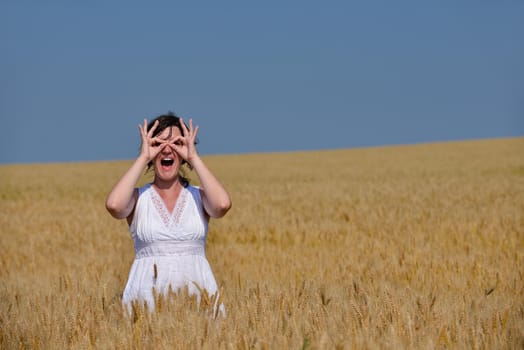 Young woman standing jumping and running  on a wheat field with blue sky the background at summer day representing healthy life and agriculture concept