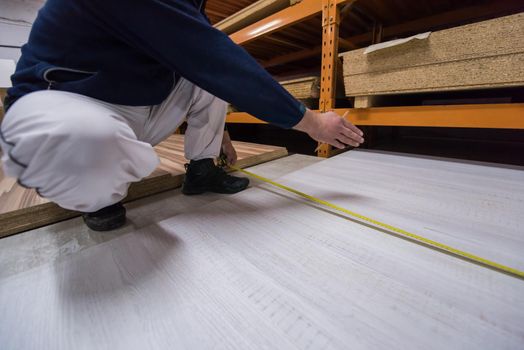 young man carpenter measuring wooden board for cutting while working in big modern carpentry High quality wood concept