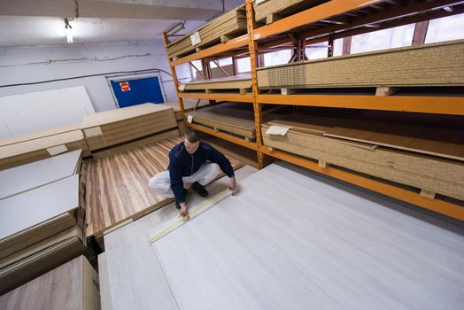 young man carpenter measuring wooden board for cutting while working in big modern carpentry High quality wood concept