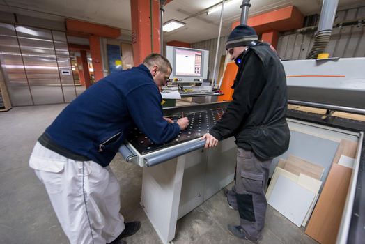 two young carpenters calculating and programming a cnc wood working machine in workshop. wood workers preparing a computer program for CNC machine at big modern carpentry