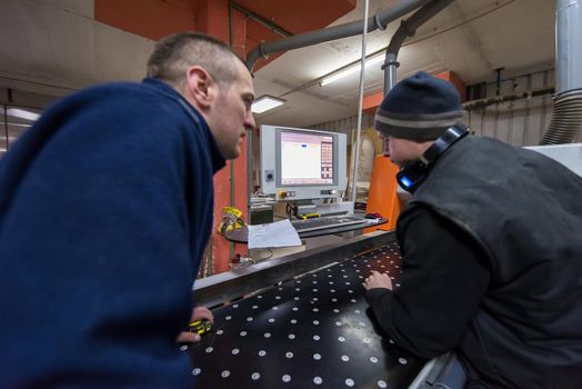 two young carpenters calculating and programming a cnc wood working machine in workshop. wood workers preparing a computer program for CNC machine at big modern carpentry