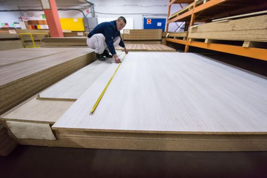 young man carpenter measuring wooden board for cutting while working in big modern carpentry High quality wood concept