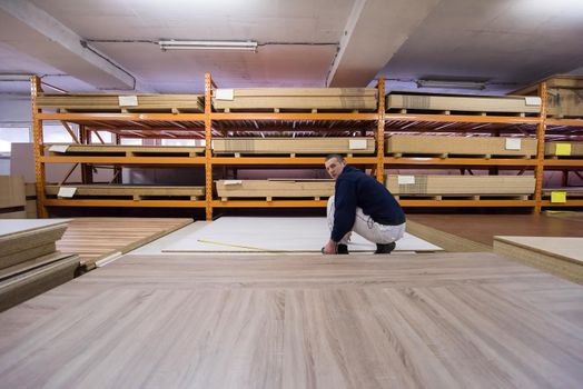 young man carpenter measuring wooden board for cutting while working in big modern carpentry High quality wood concept