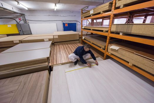 young man carpenter measuring wooden board for cutting while working in big modern carpentry High quality wood concept