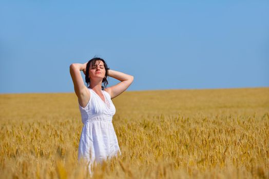 Young woman standing jumping and running  on a wheat field with blue sky the background at summer day representing healthy life and agriculture concept