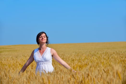 Young woman standing jumping and running  on a wheat field with blue sky the background at summer day representing healthy life and agriculture concept