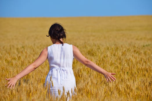 Young woman standing jumping and running  on a wheat field with blue sky the background at summer day representing healthy life and agriculture concept