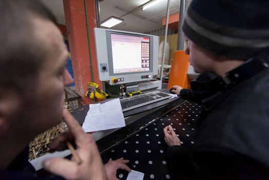 two young carpenters calculating and programming a cnc wood working machine in workshop. wood workers preparing a computer program for CNC machine at big modern carpentry