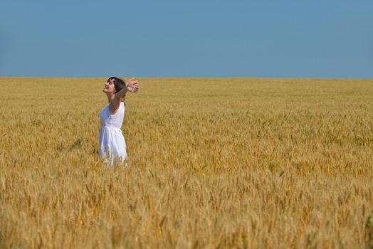 Young woman standing jumping and running  on a wheat field with blue sky in  background at summer day representing healthy life and agriculture concept