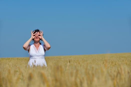 Young woman standing jumping and running  on a wheat field with blue sky the background at summer day representing healthy life and agriculture concept