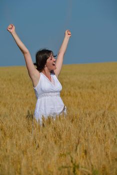 Young woman standing jumping and running  on a wheat field with blue sky in  background at summer day representing healthy life and agriculture concept