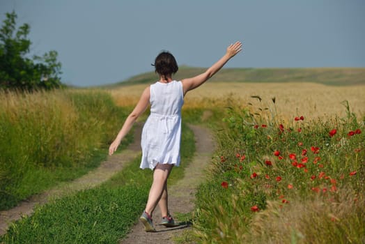 Young woman standing jumping and running  on a wheat field with blue sky in  background at summer day representing healthy life and agriculture concept