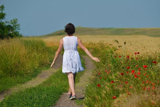 Young woman standing jumping and running  on a wheat field with blue sky in  background at summer day representing healthy life and agriculture concept