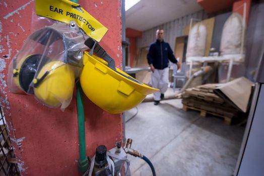 standard security equipment yellow helmet and ears protection hanging on the wall at production Department of a big modern wooden furniture factory