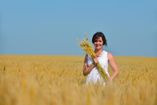 Young woman standing jumping and running  on a wheat field with blue sky the background at summer day representing healthy life and agriculture concept