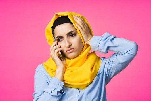 muslim woman in yellow hijab talking on the phone technology pink background. High quality photo