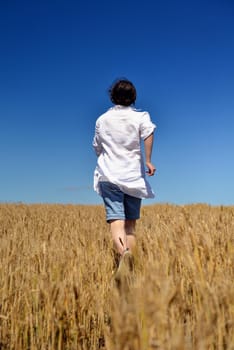 Young woman standing jumping and running  on a wheat field with blue sky in  background at summer day representing healthy life and agriculture concept