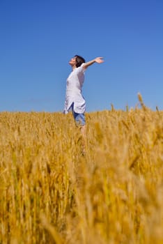 Young woman standing jumping and running  on a wheat field with blue sky the background at summer day representing healthy life and agriculture concept