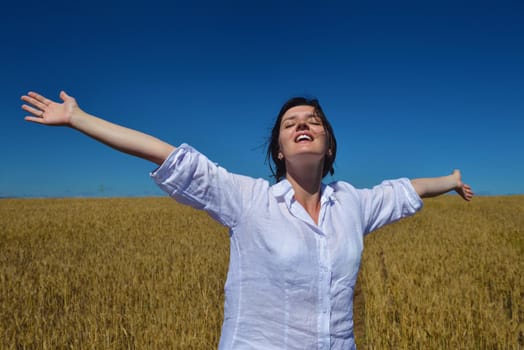 Young woman standing jumping and running  on a wheat field with blue sky in  background at summer day representing healthy life and agriculture concept