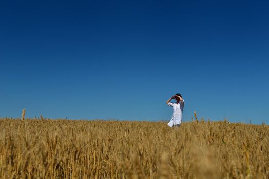 Young woman standing jumping and running  on a wheat field with blue sky in  background at summer day representing healthy life and agriculture concept