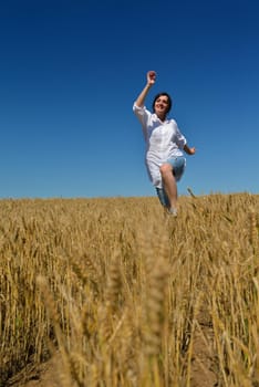 Young woman standing jumping and running  on a wheat field with blue sky in  background at summer day representing healthy life and agriculture concept