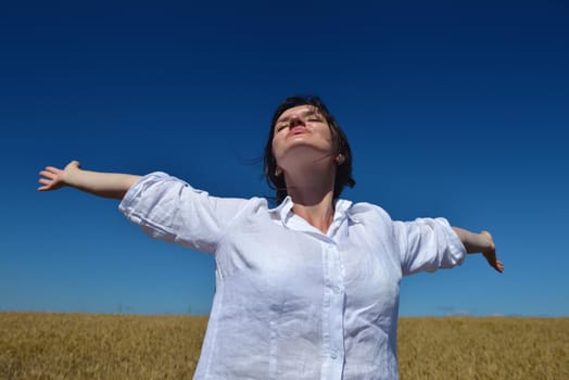 Young woman standing jumping and running  on a wheat field with blue sky in  background at summer day representing healthy life and agriculture concept