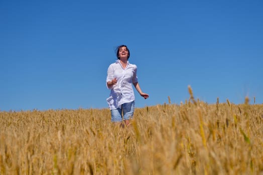 Young woman standing jumping and running  on a wheat field with blue sky the background at summer day representing healthy life and agriculture concept