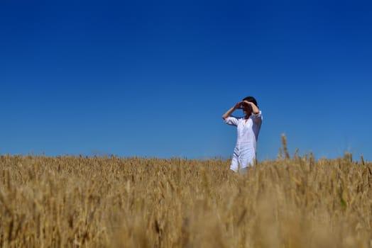 Young woman standing jumping and running  on a wheat field with blue sky in  background at summer day representing healthy life and agriculture concept