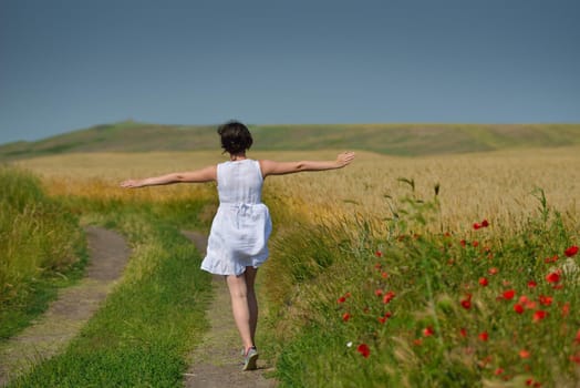 Young woman standing jumping and running  on a wheat field with blue sky the background at summer day representing healthy life and agriculture concept