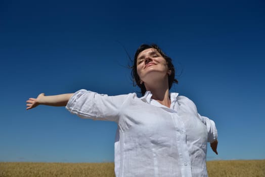 Young woman standing jumping and running  on a wheat field with blue sky the background at summer day representing healthy life and agriculture concept