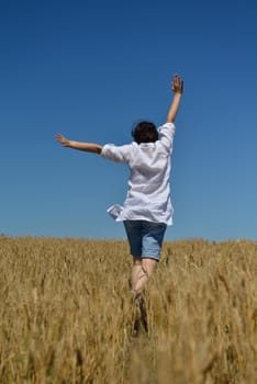 Young woman standing jumping and running  on a wheat field with blue sky the background at summer day representing healthy life and agriculture concept