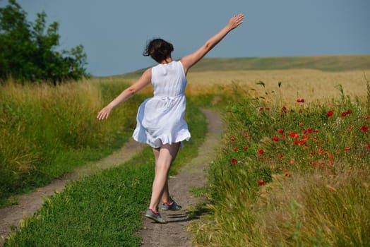 Young woman standing jumping and running  on a wheat field with blue sky the background at summer day representing healthy life and agriculture concept